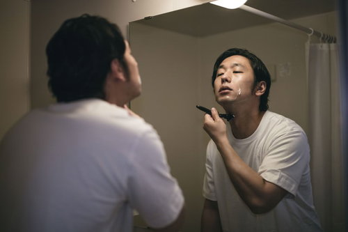 シェービングの最後の仕上げをする髭男性、洗面所で丁寧に髭剃り