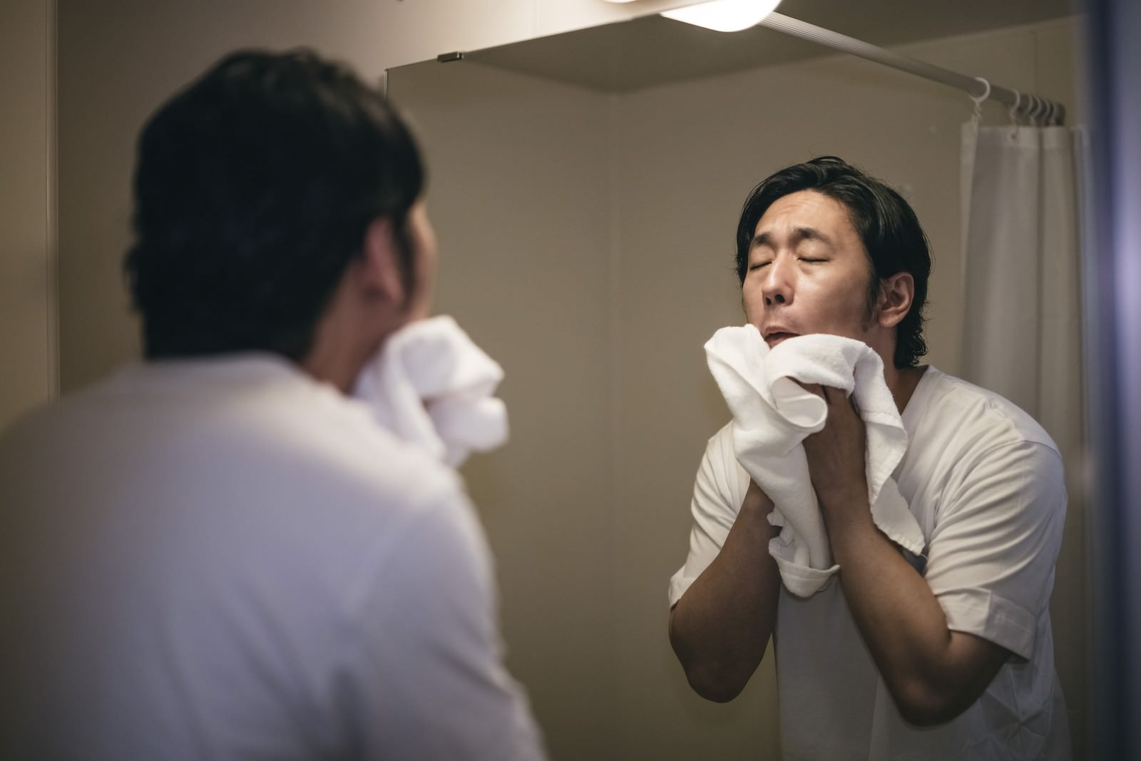 バスルームで白いタオルを使って顔を拭く男性［モデル：大川竜弥］