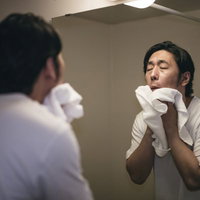 洗顔後に白いタオルで顔を拭く男性のスキンケアの写真