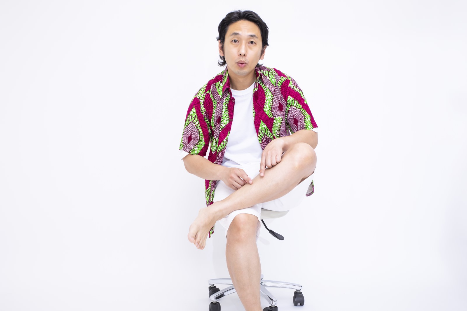 椅子に座りすね毛処理をした足を見せて笑顔の柄シャツの男性［モデル：大川竜弥］