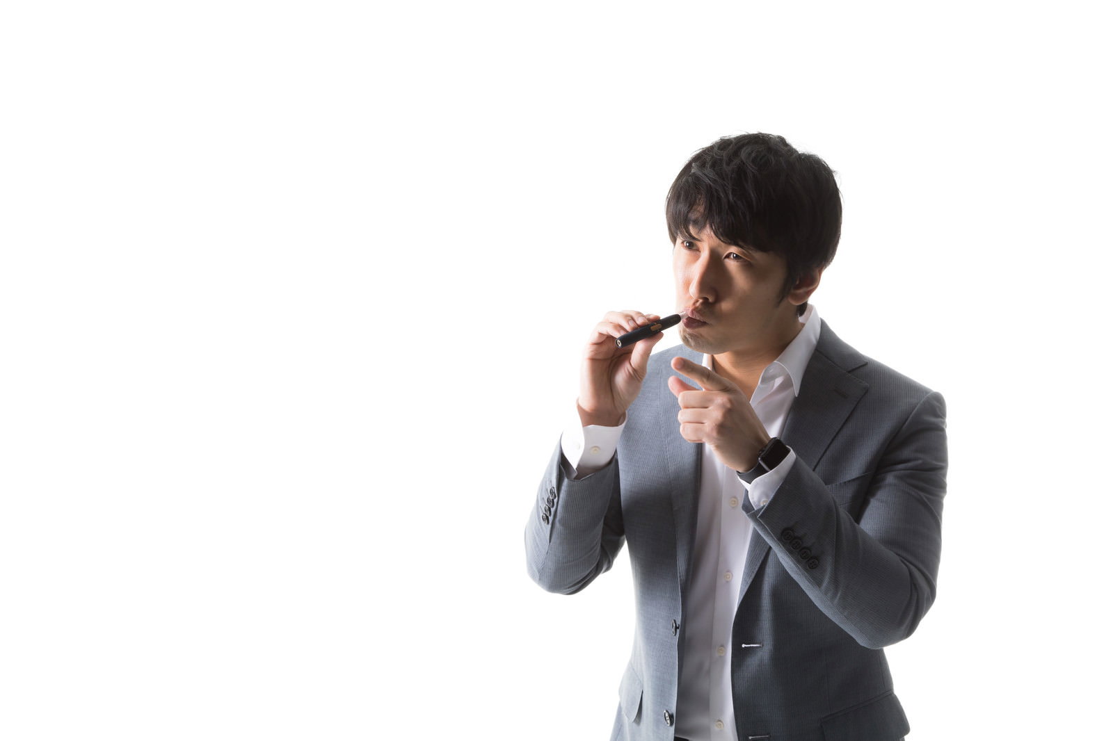 加熱式たばこを口にくわえながら指差し確認をするグレーのスーツを着た男性［モデル：大川竜弥］