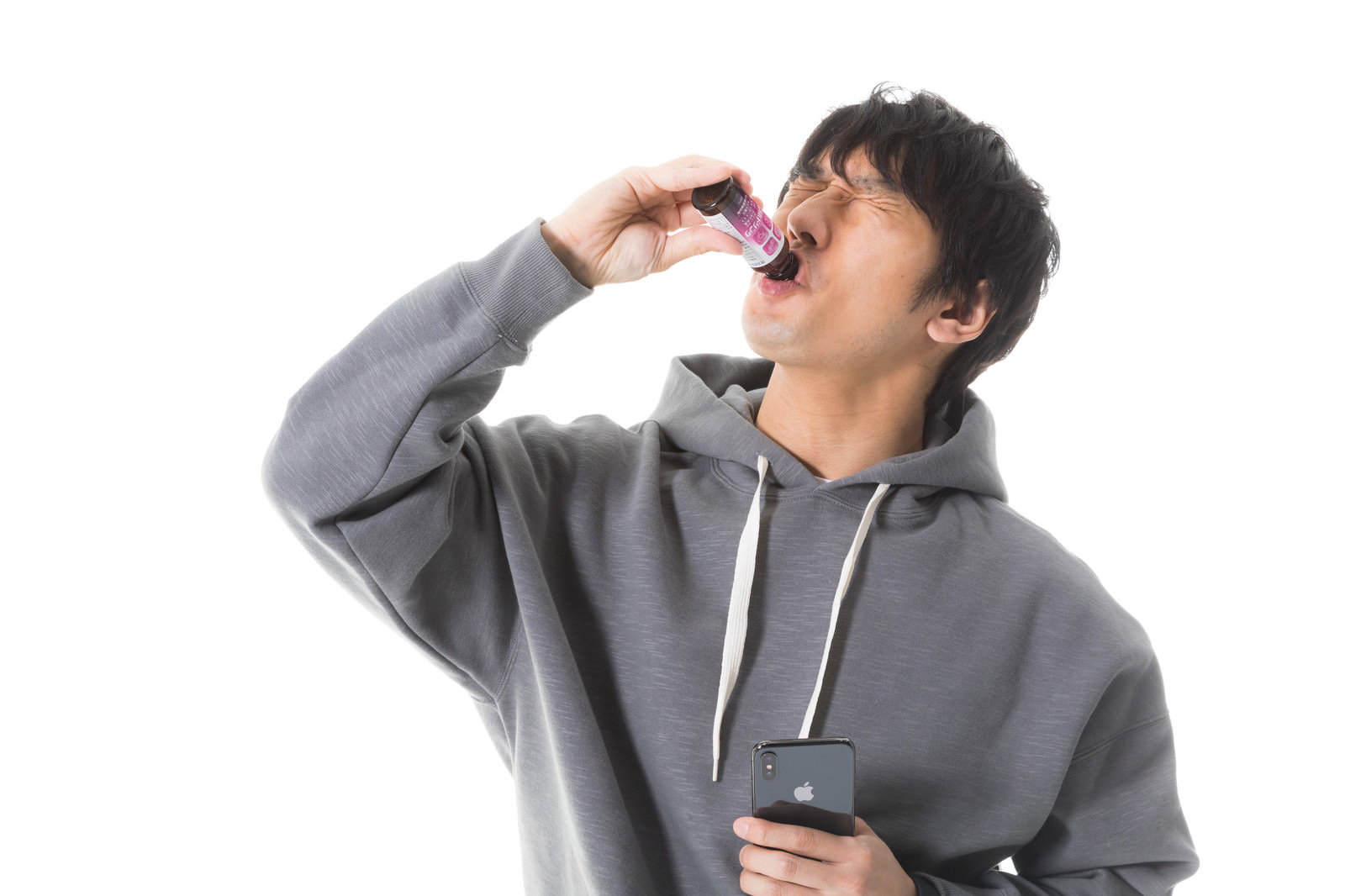 グレーのパーカーを着た男性が栄養ドリンクを飲んでいる様子［モデル：大川竜弥］