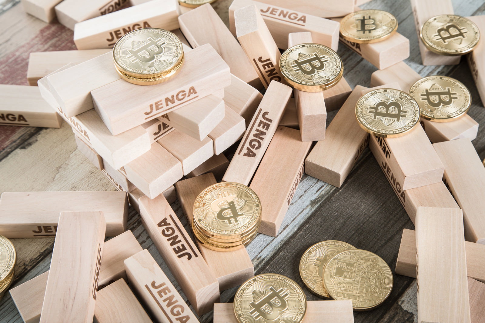 崩れ落ちた木製ジェンガブロックと金色のビットコインコインが散らばっている様子