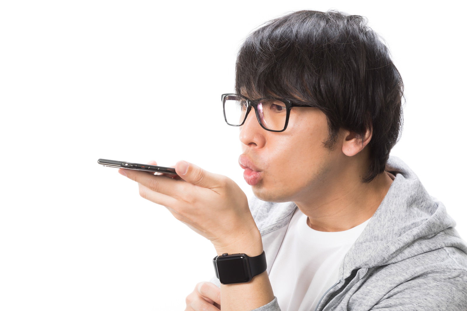 スマートフォンのマイクに話しかける眼鏡の男性［モデル：大川竜弥］