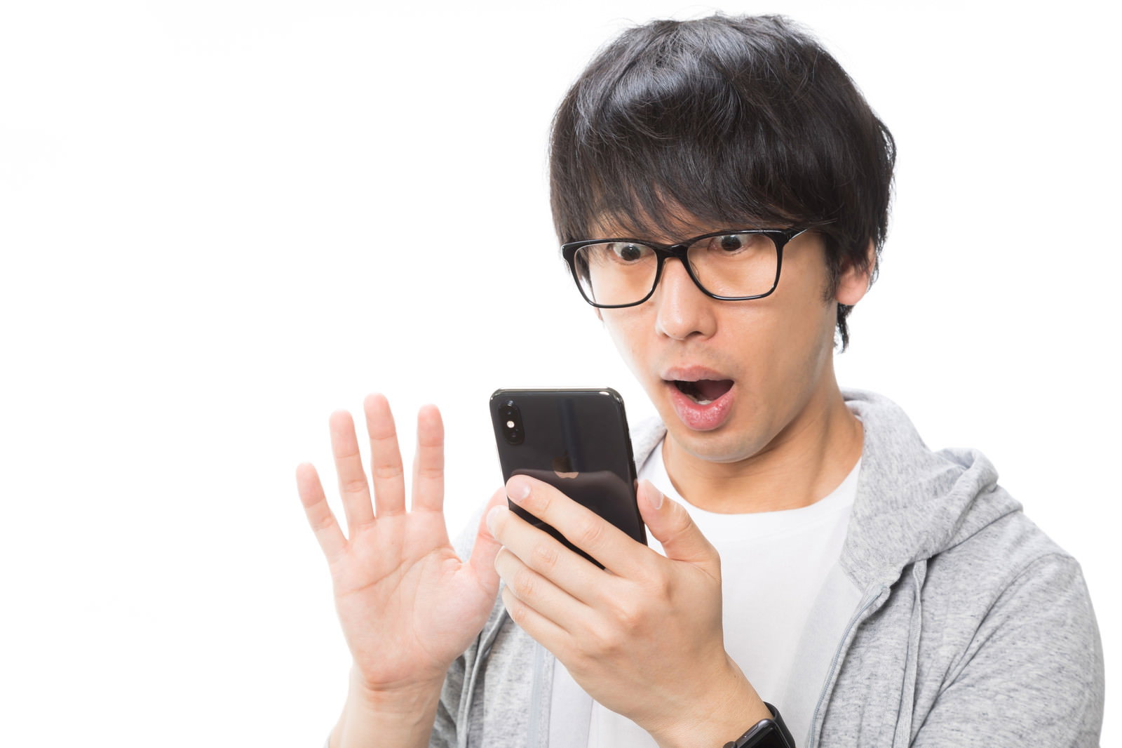 黒いスマートフォンを見て目を丸くして驚いている眼鏡をかけた男性［モデル：大川竜弥］