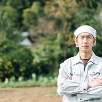 脱サラして農家はじめました、白いヘッドバンド姿で畑に立つ男性の写真