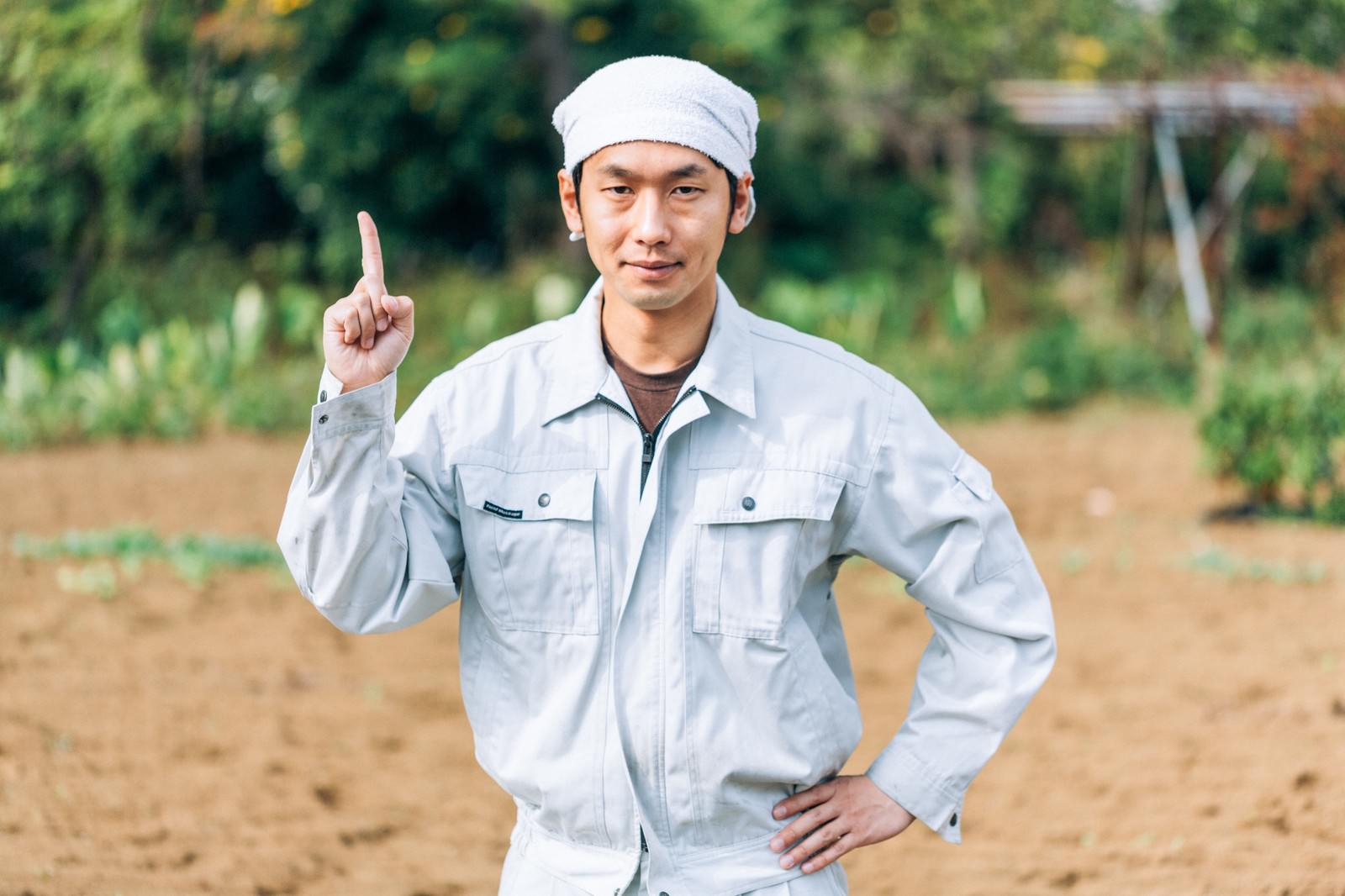 白い作業着を着た農家の男性が、指をさして説明するポーズをとっている［モデル：大川竜弥］