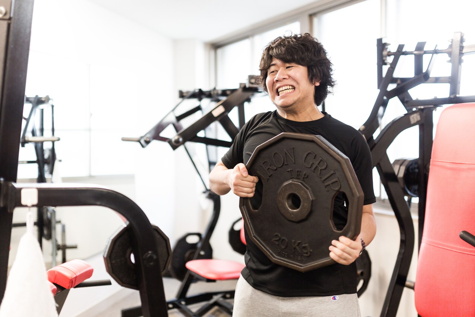 ジムで20kgウェイトプレートを抱えて笑う男性［モデル：あまのじゃく］