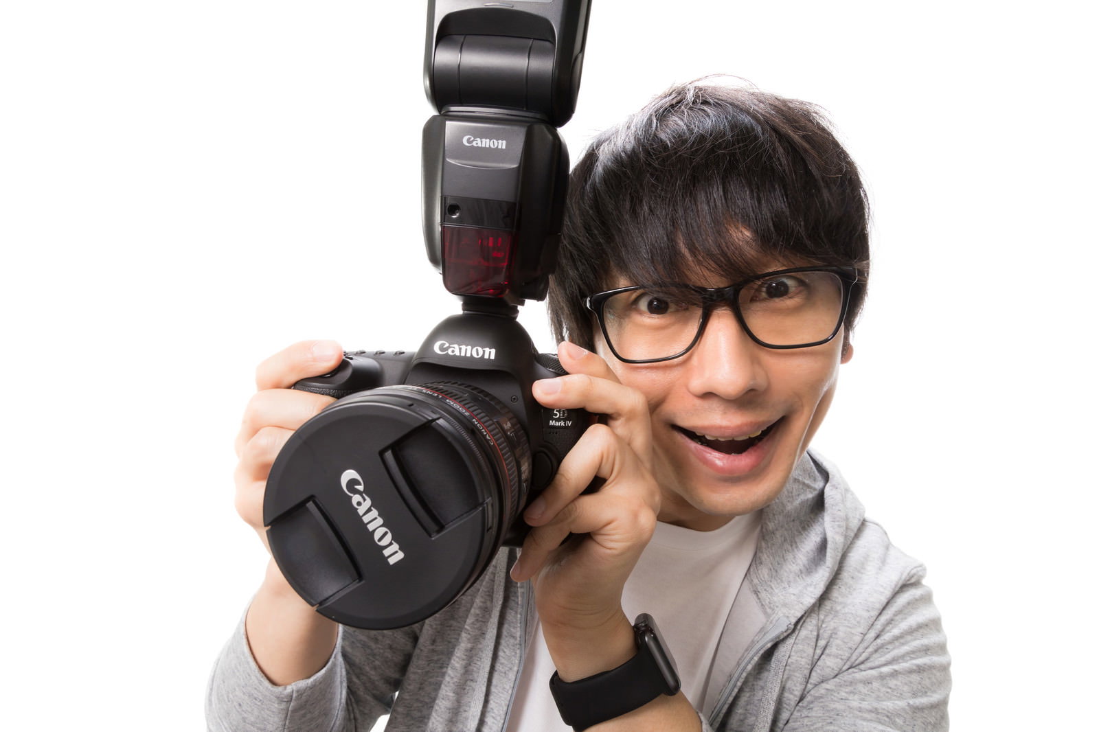 デジタル一眼レフカメラとストロボを持ち笑顔で構える眼鏡の男性［モデル：大川竜弥］