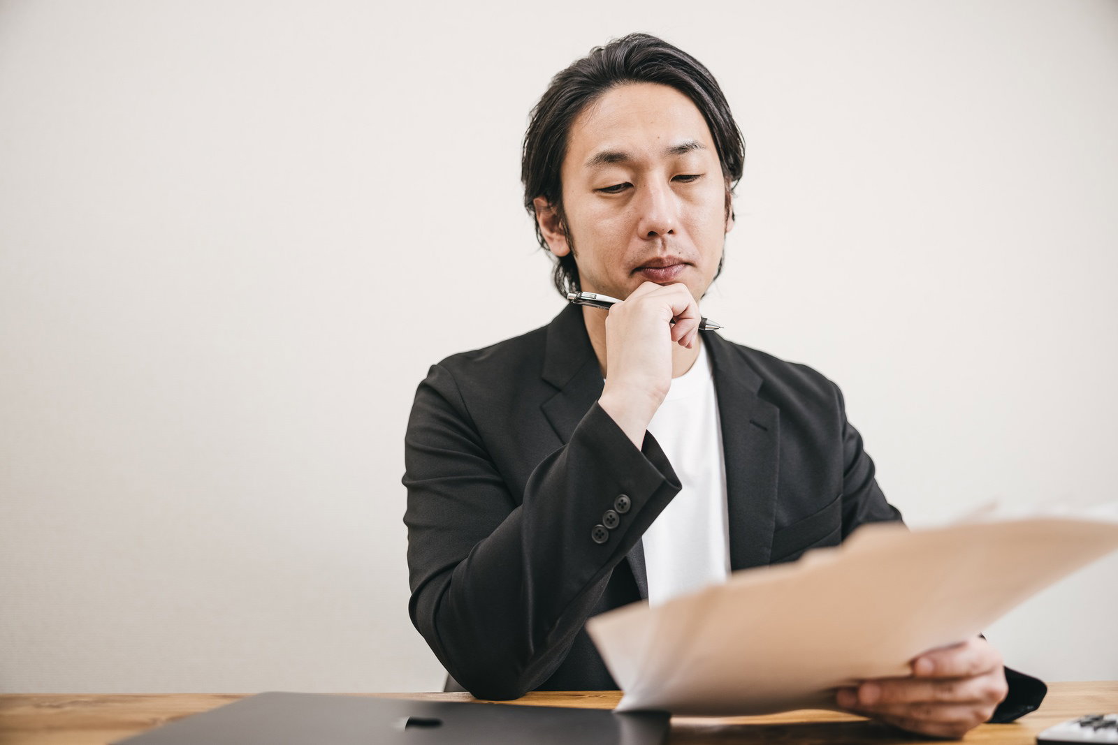 書類を見ながら頬杖をついて考え込む面接官の男性［モデル：大川竜弥］