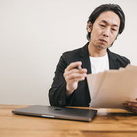 書類選考で悩む面接官の男性が候補者の書類を審査検討している場面の写真