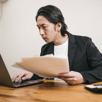 資料をパソコンで見比べてチェックする男性の写真