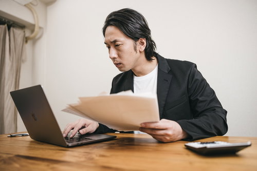 資料をパソコンで見比べてチェックする男性