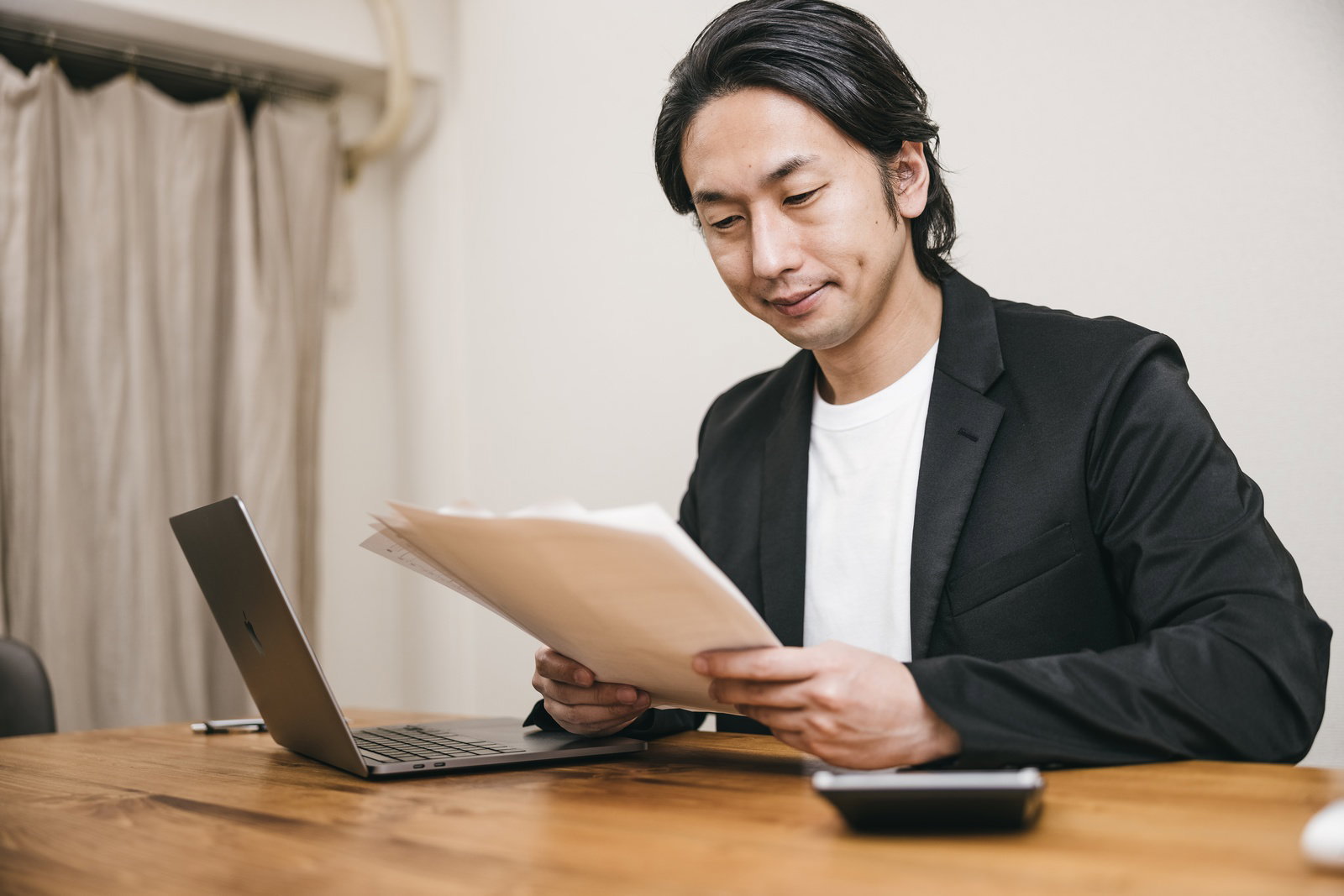 木製デスクで書類を読む黒いスーツの男性審査員［モデル：大川竜弥］