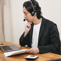 ヘッドセットを装着してリモートワークする男性の写真