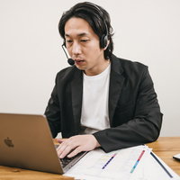 ノートパソコンを操作しながらヘッドセットを着用して在宅勤務中の男性の写真