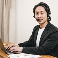 ヘッドセットを着けてパソコン作業をするテレワーク中の笑顔の男性の写真