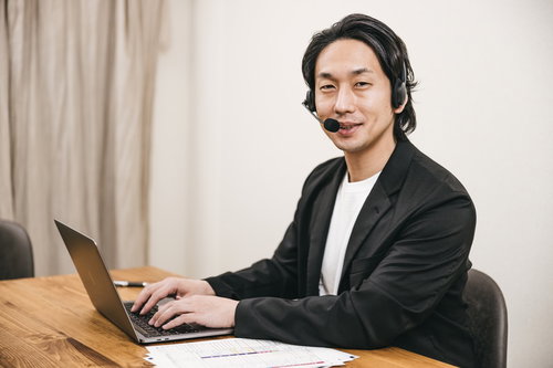 ヘッドセットを着けてパソコン作業をするテレワーク中の笑顔の男性