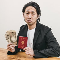 札束とパスポートを手に持つスーツ姿の男性の写真