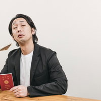 パスポートを持ちながら一万円札を団扇代わりにする男性の写真