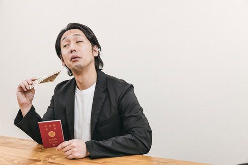パスポートを持ちながら一万円札を団扇代わりにする男性