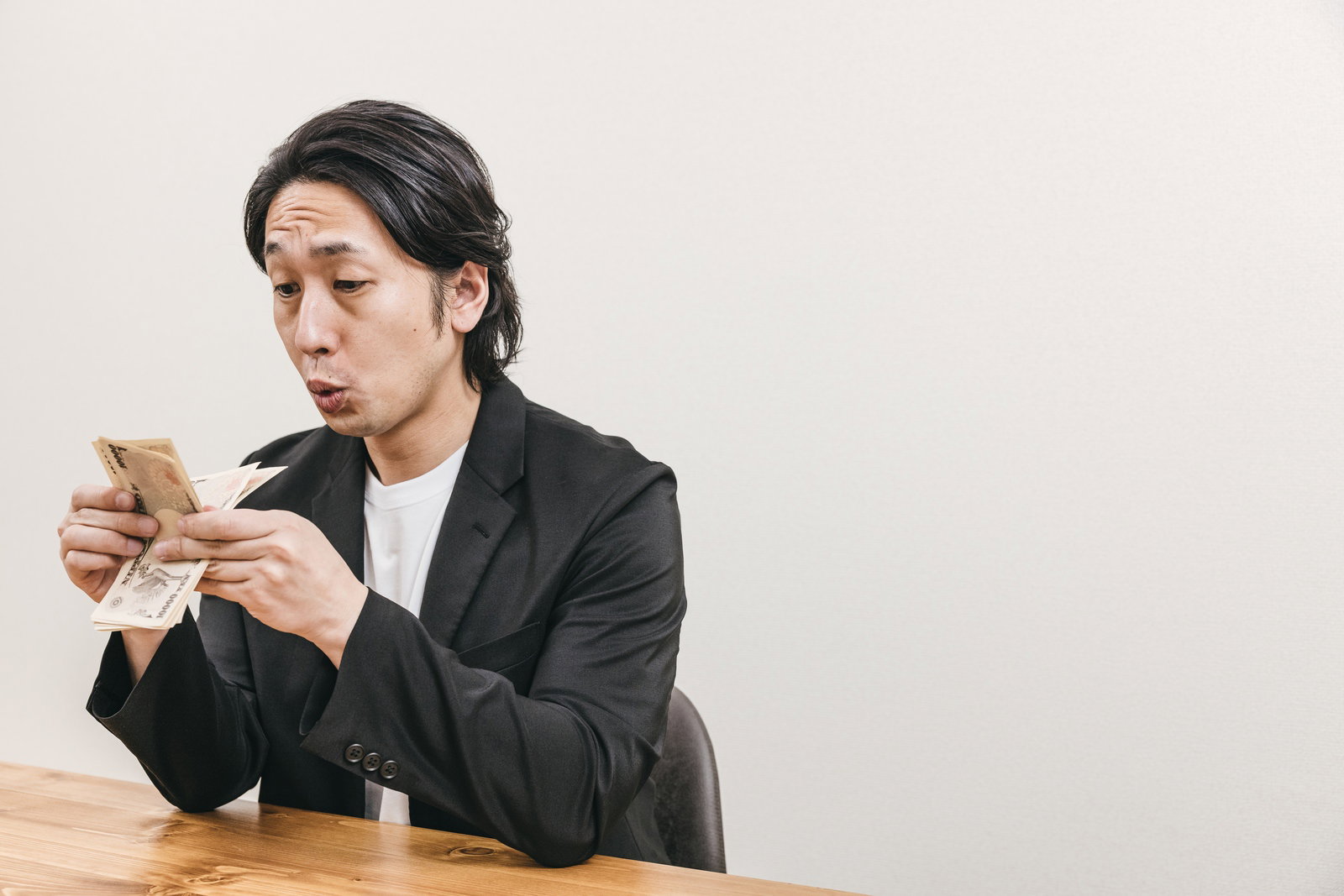 木製テーブルでお金を数えるスーツ姿の男性［モデル：大川竜弥］