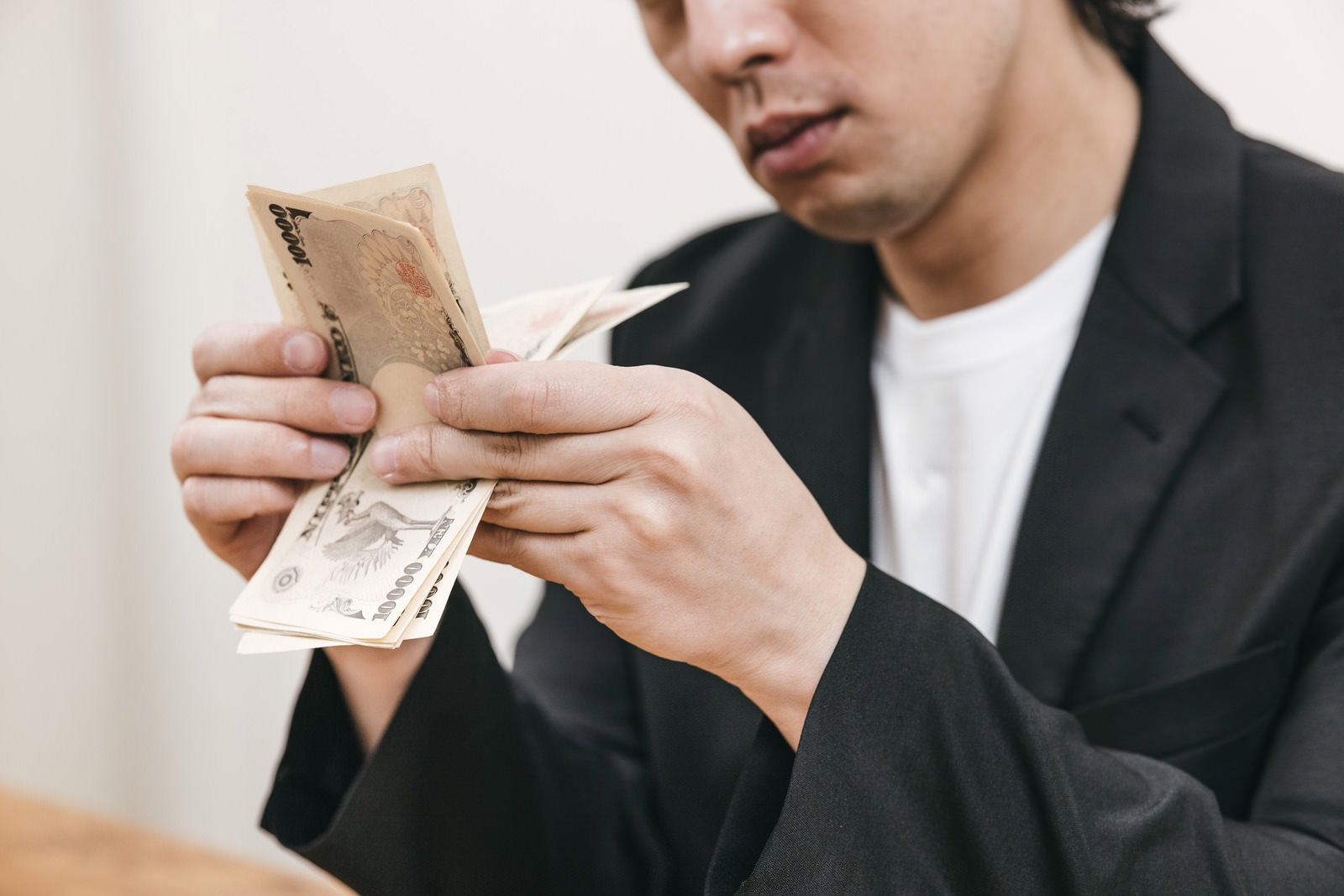 スーツを着た男性が一万円札を手に取り札勘をしている［モデル：大川竜弥］
