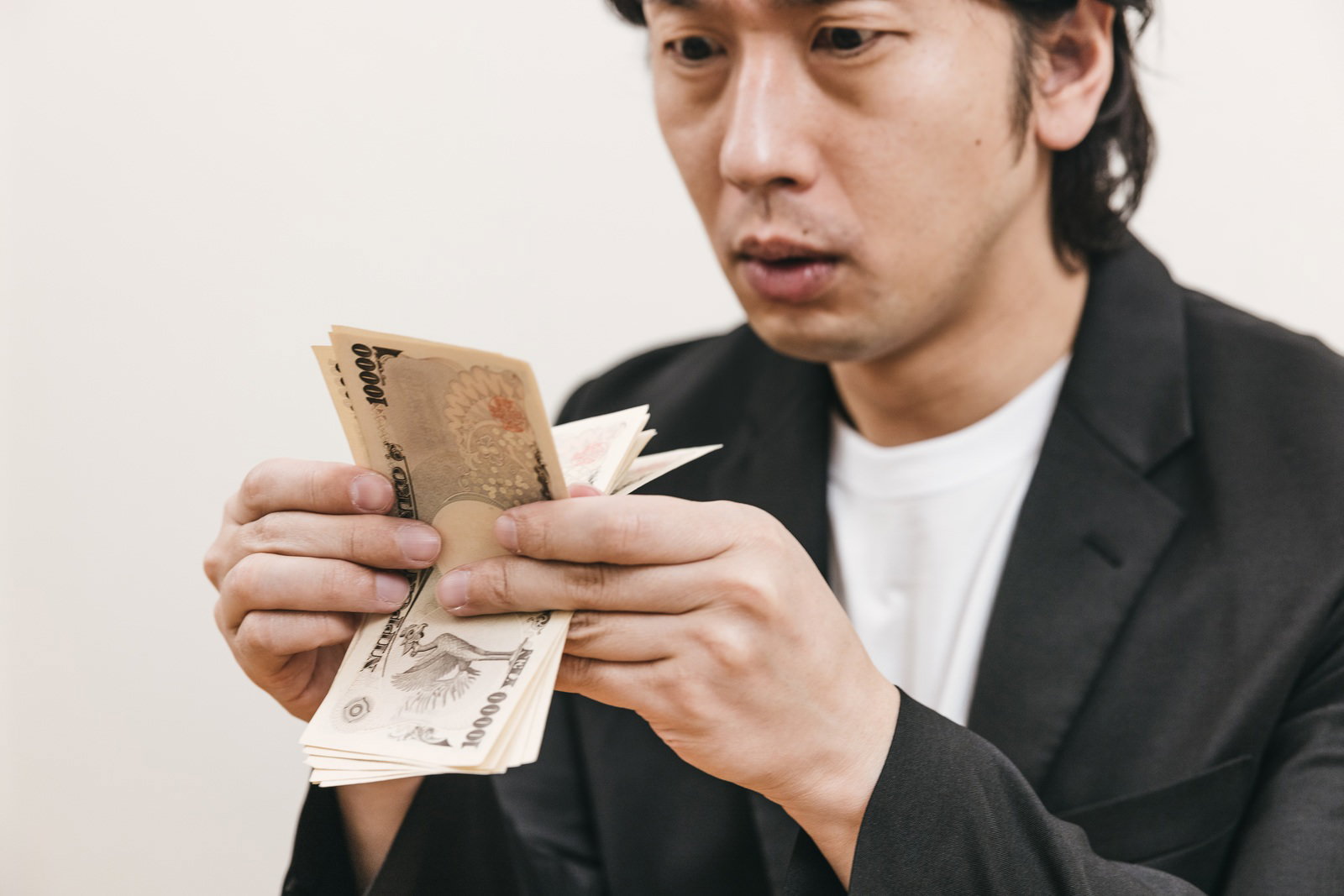 黒いジャケットを着た男性が一万円札を手に持ち札勘している［モデル：大川竜弥］