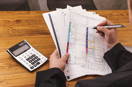確定申告書を片手にペンを持つ手と卓上の電卓