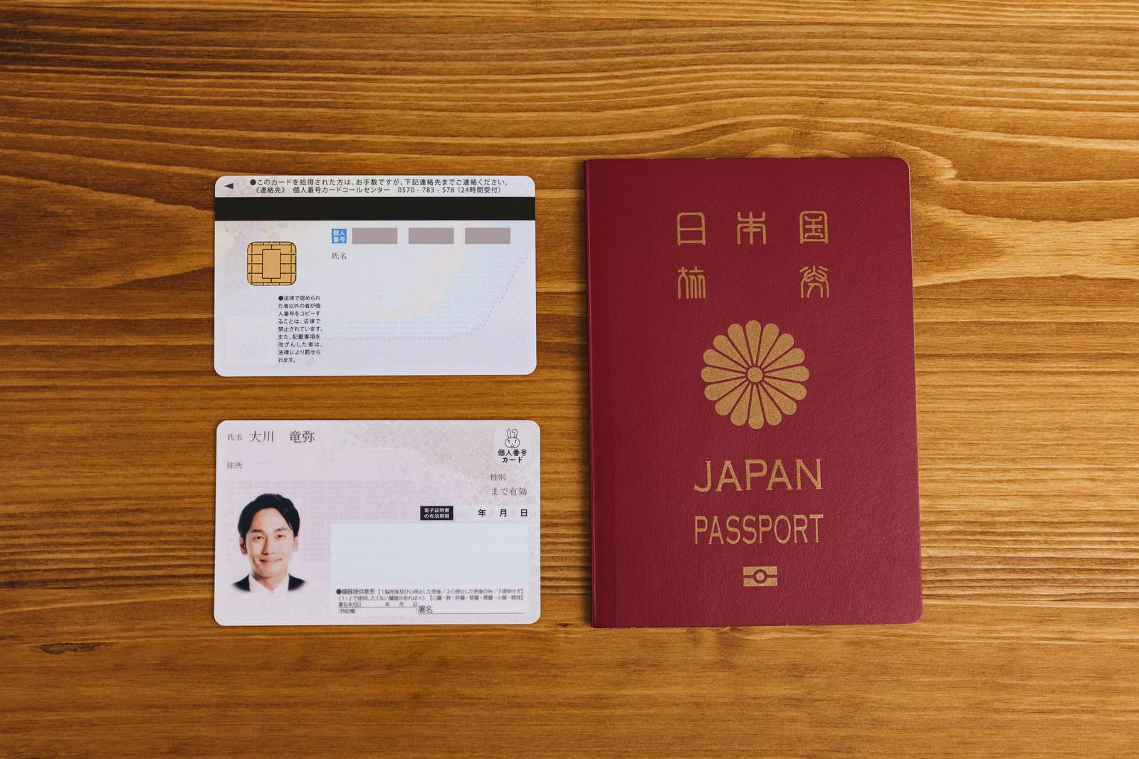 木目調のテーブルに置かれた日本のパスポートとマイナンバーカード［モデル：大川竜弥］