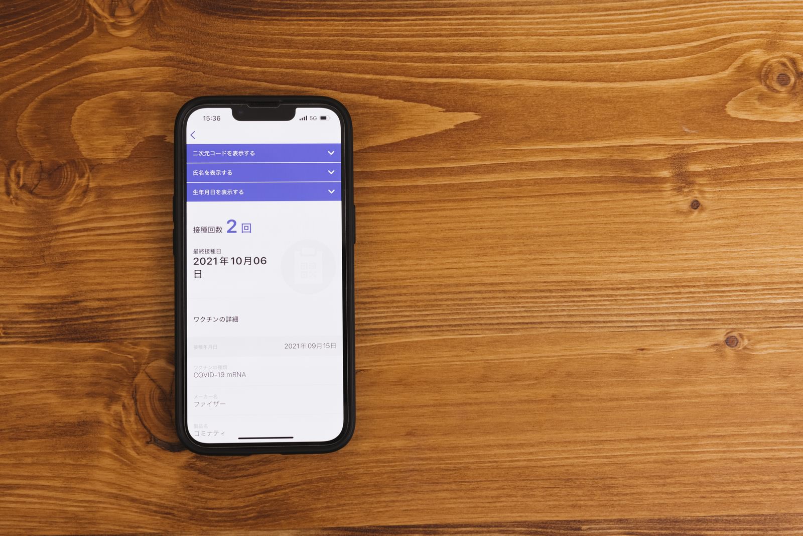 木目のテーブルに置かれたスマートフォンにワクチン接種証明書アプリが表示されている様子