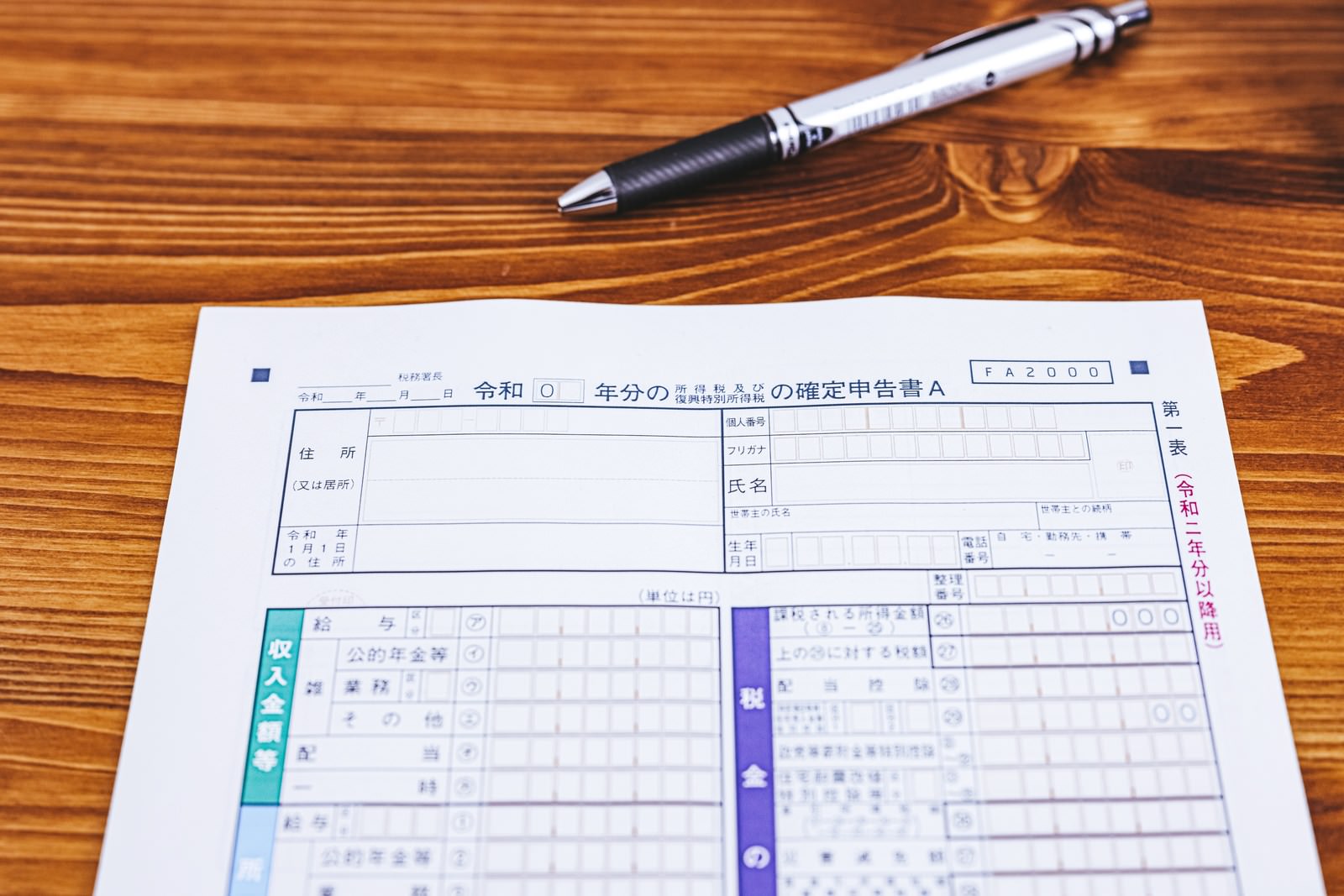 木製テーブルの上に置かれた白紙の確定申告書とボールペン