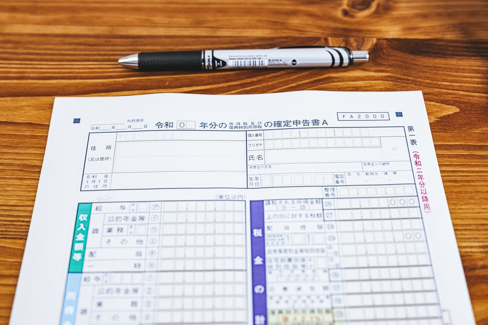 木目テーブルに置かれた確定申告書と黒いペン