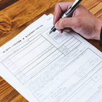 木目テーブルで個人番号カード交付申請書にペンで記入中の写真
