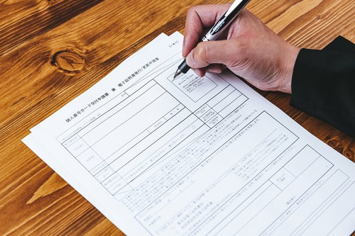 木目テーブルで個人番号カード交付申請書にペンで記入中