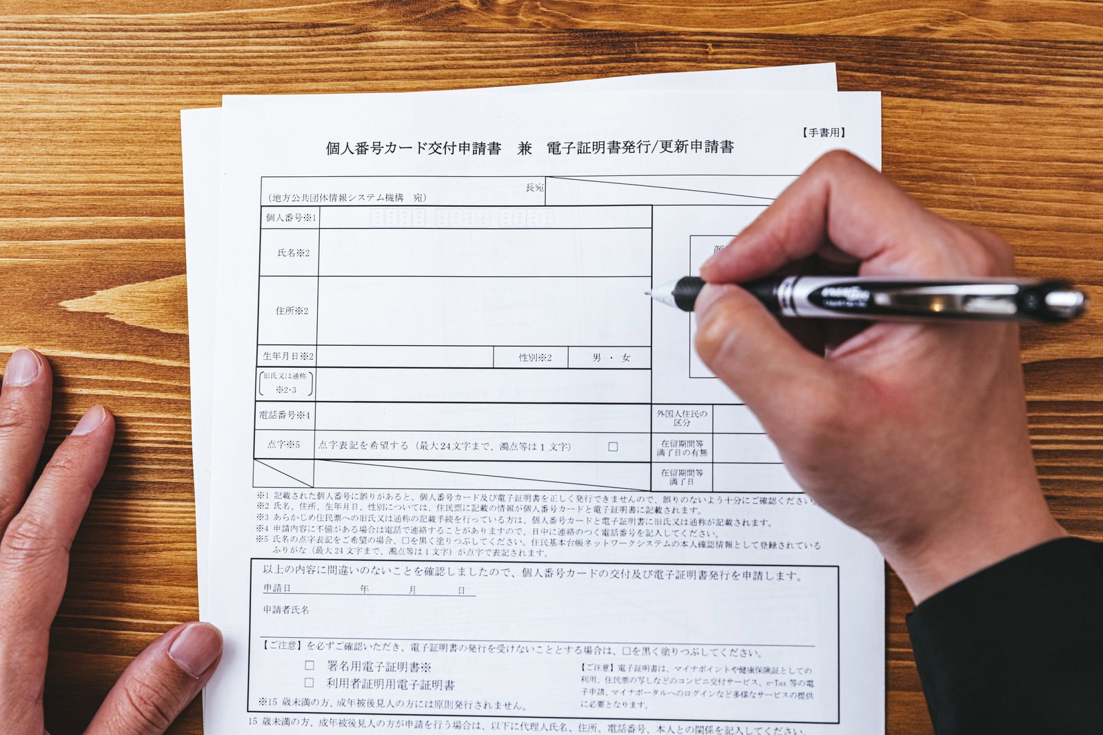 個人番号カード交付申請書に黒いペンで記入している手元