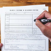 個人番号カード交付申請書に黒いペンで記載中の写真