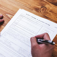 木製テーブルで個人番号カード交付申請書にペンで記入するの写真