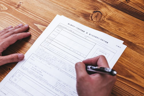 木製テーブルで個人番号カード交付申請書にペンで記入する