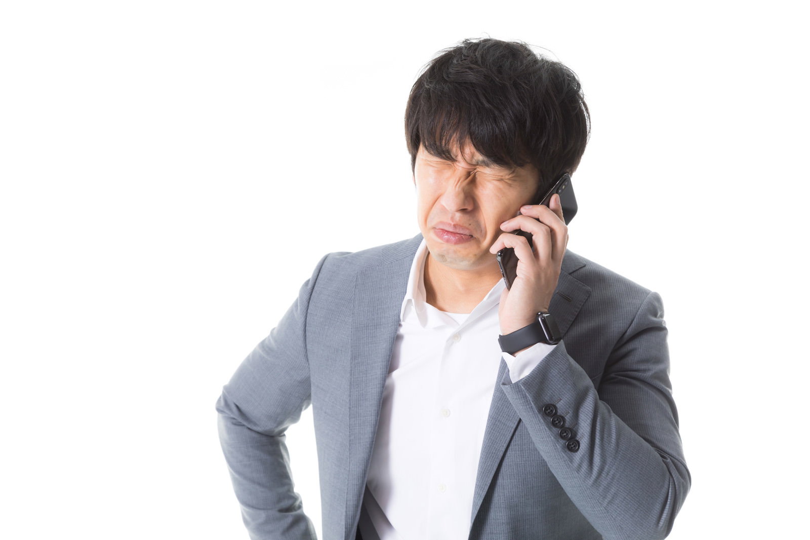 グレーのスーツを着た男性が携帯電話で通話しながら涙目で困った表情をしている［モデル：大川竜弥］