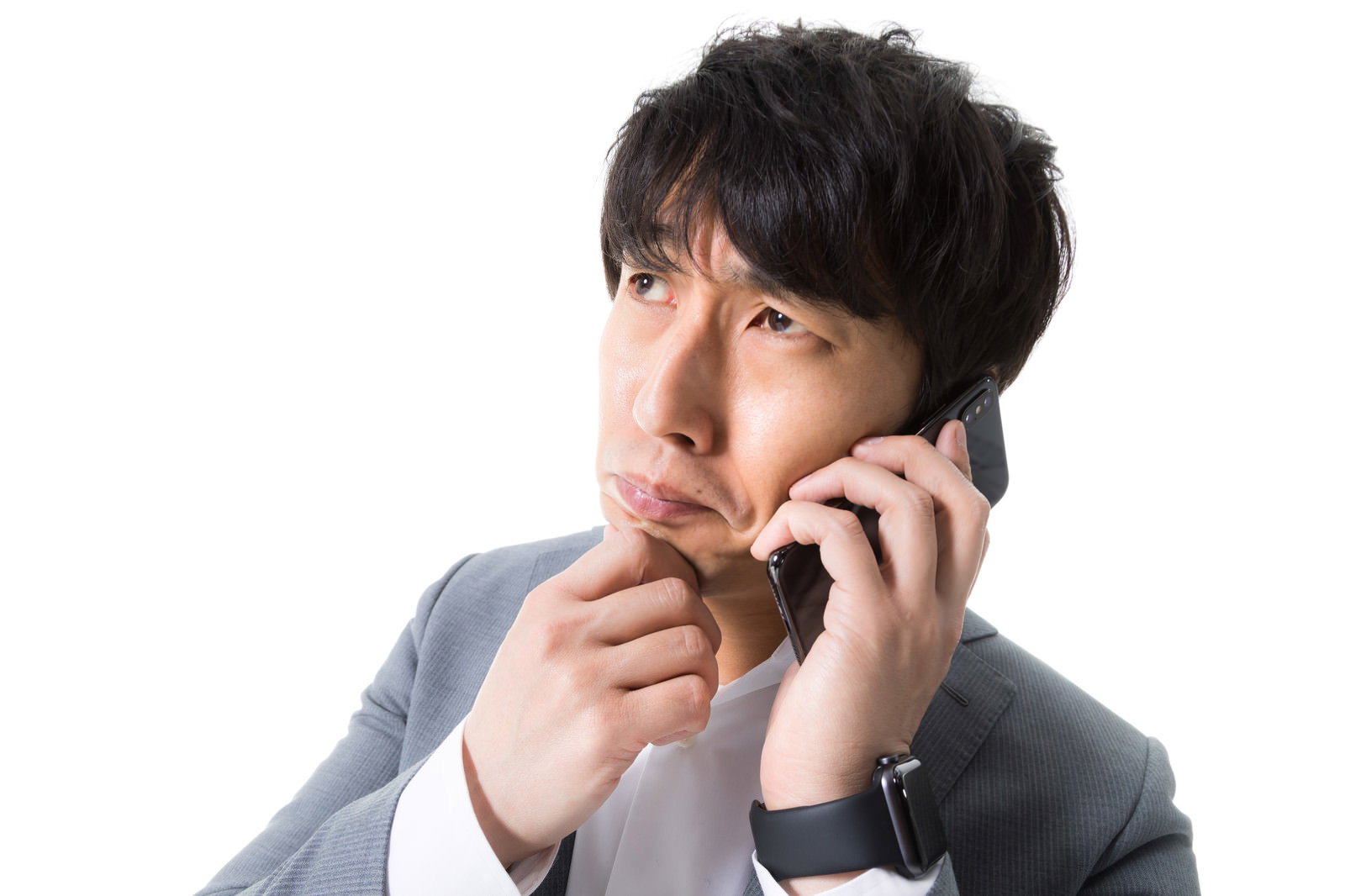 グレースーツの男性が携帯電話で通話しながら顎に指を当てて悩んでいる［モデル：大川竜弥］