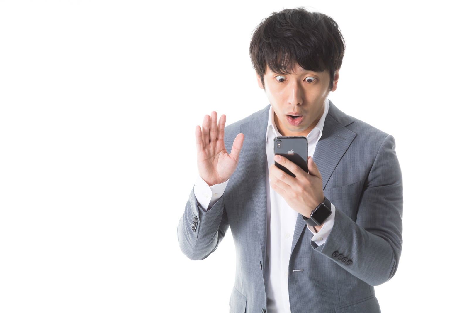 スマートフォンを見て片手を上げて驚く表情のグレースーツの男性［モデル：大川竜弥］