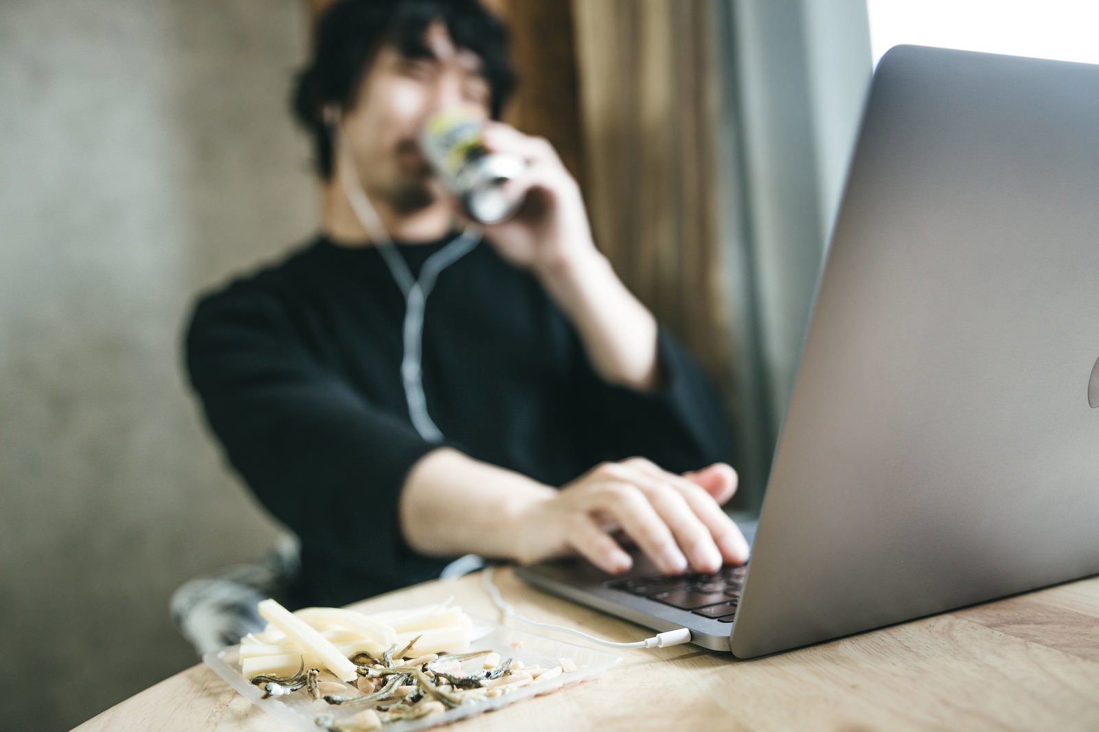 パソコンでリモート飲み会をしながらおつまみを食べる男性［モデル：大川竜弥］