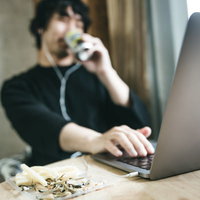 おつまみを食べながらリモート飲み会をする男性の写真