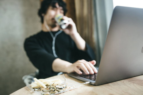 おつまみを食べながらリモート飲み会をする男性