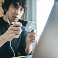 PC画面をスマホで撮影する男性のデスクワーク風景の写真