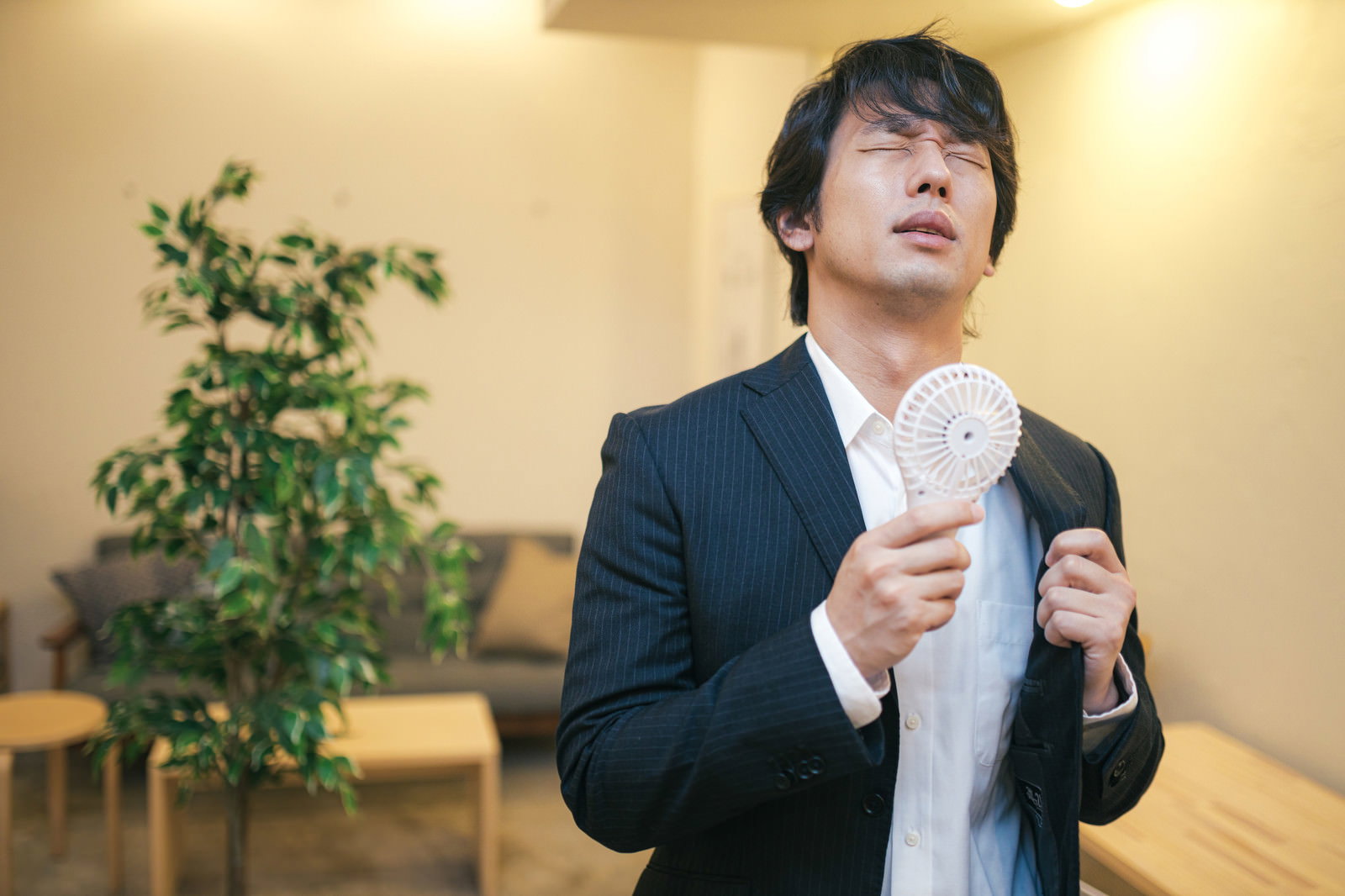 スーツ姿の営業マンがハンディ扇風機を使用している様子［モデル：大川竜弥］