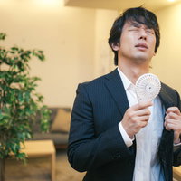 スーツ姿の営業マンが使うハンディ扇風機で暑さ対策の写真