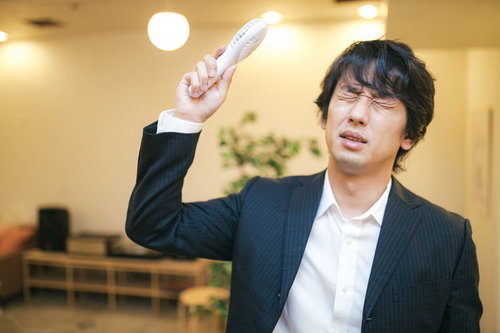 ハンディ扇風機で髪の毛を乾かそうとする黒いスーツ姿の男性