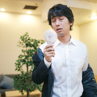 オフィスの冷房が壊れて手持ち扇風機で涼む男性の写真